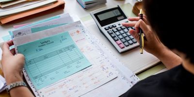 Mulher digitando na calculadora enquanto faz contas nos papéis