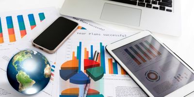 Computador, celular, Tablet, e gráficos em papéis em cima de uma mesa